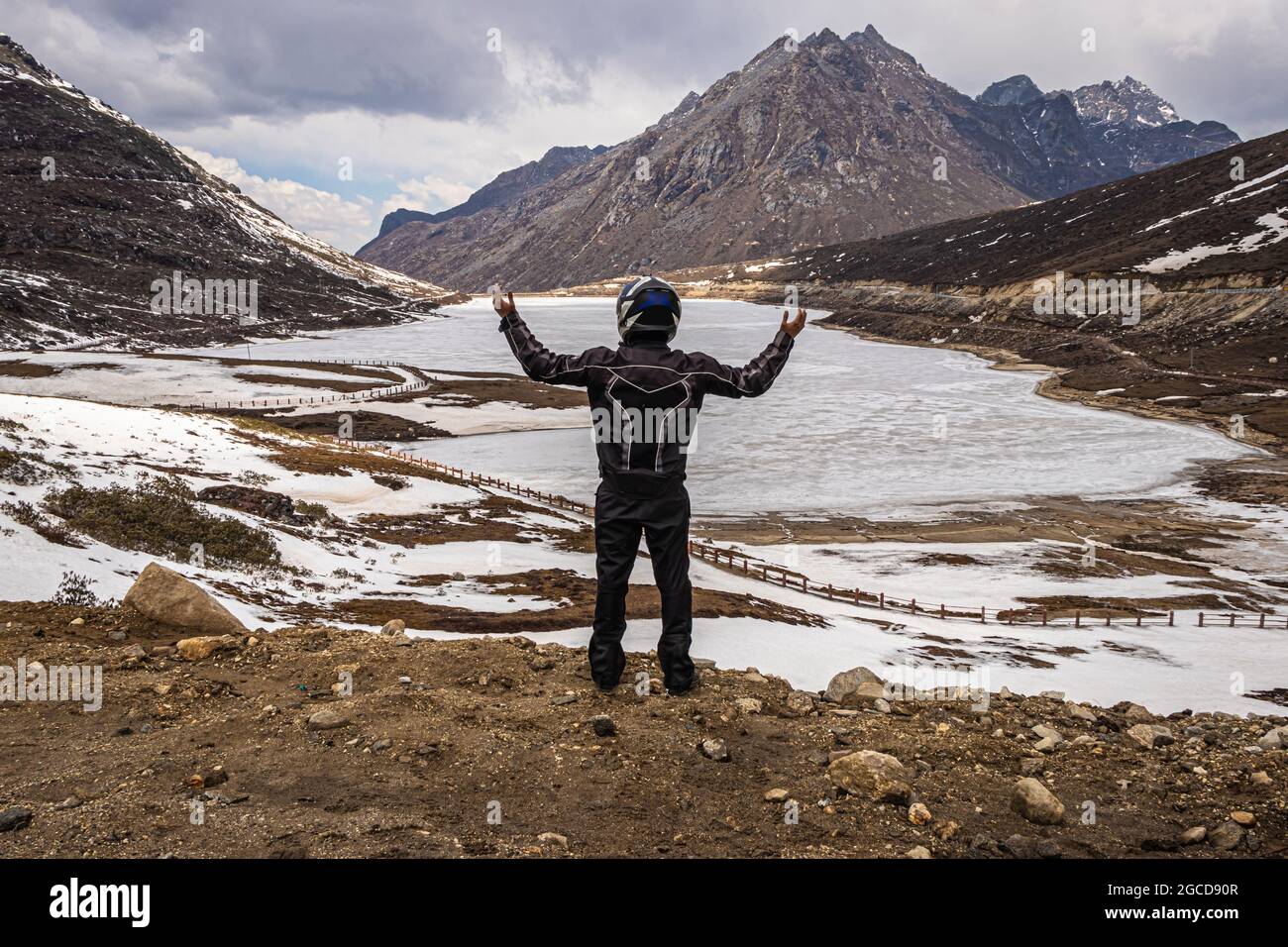 joven hombre biker viajero en solitario en el lago congelado con fondo del valle de montaña en el día de la imagen se toma en el paso de sela tawang arunachal pradesh india. Foto de stock