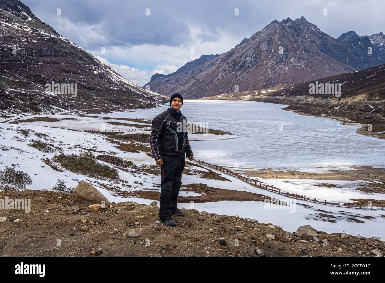 joven hombre biker viajero en solitario en el lago congelado con fondo del valle de montaña en el día de la imagen se toma en el paso de sela tawang arunachal pradesh india. Foto de stock