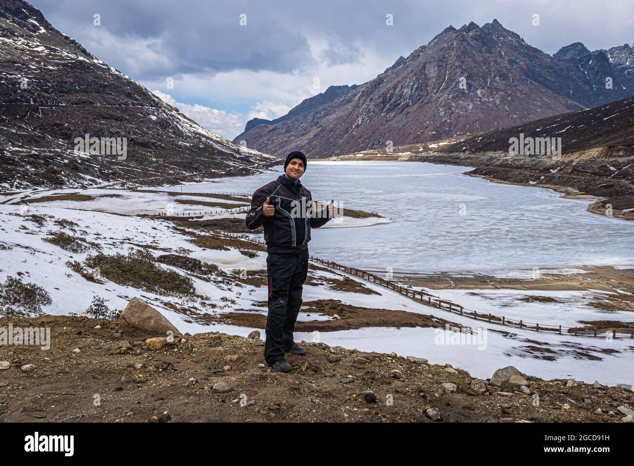 joven hombre biker viajero en solitario en el lago congelado con fondo del valle de montaña en el día de la imagen se toma en el paso de sela tawang arunachal pradesh india. Foto de stock