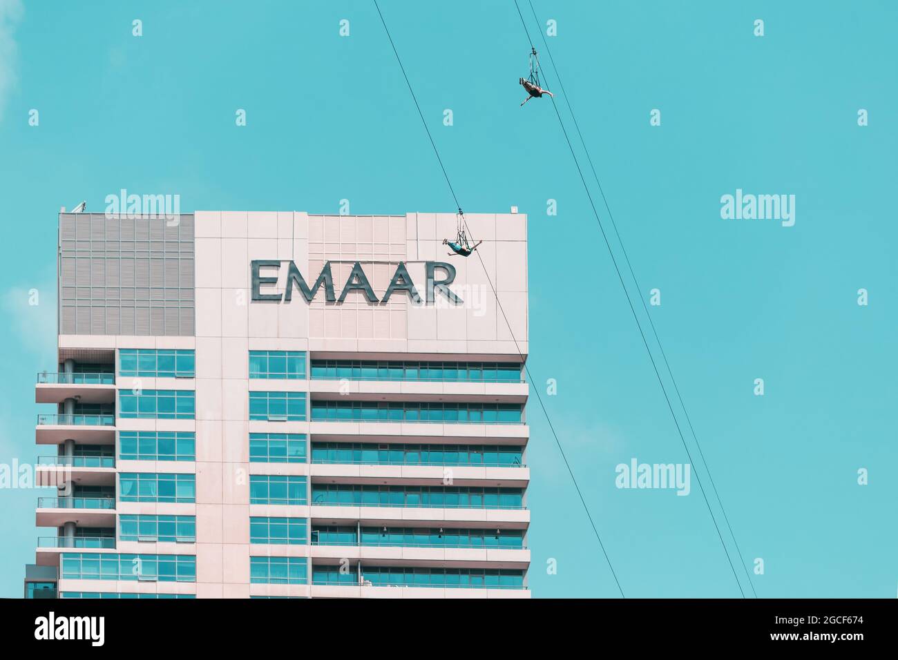 26 de febrero de 2021, Emiratos Árabes Unidos, Dubai: Dos aventureros vuelan por una cuerda de tirolina en un vuelo extremo en Dubai Marina contra el logotipo de Emaar Foto de stock