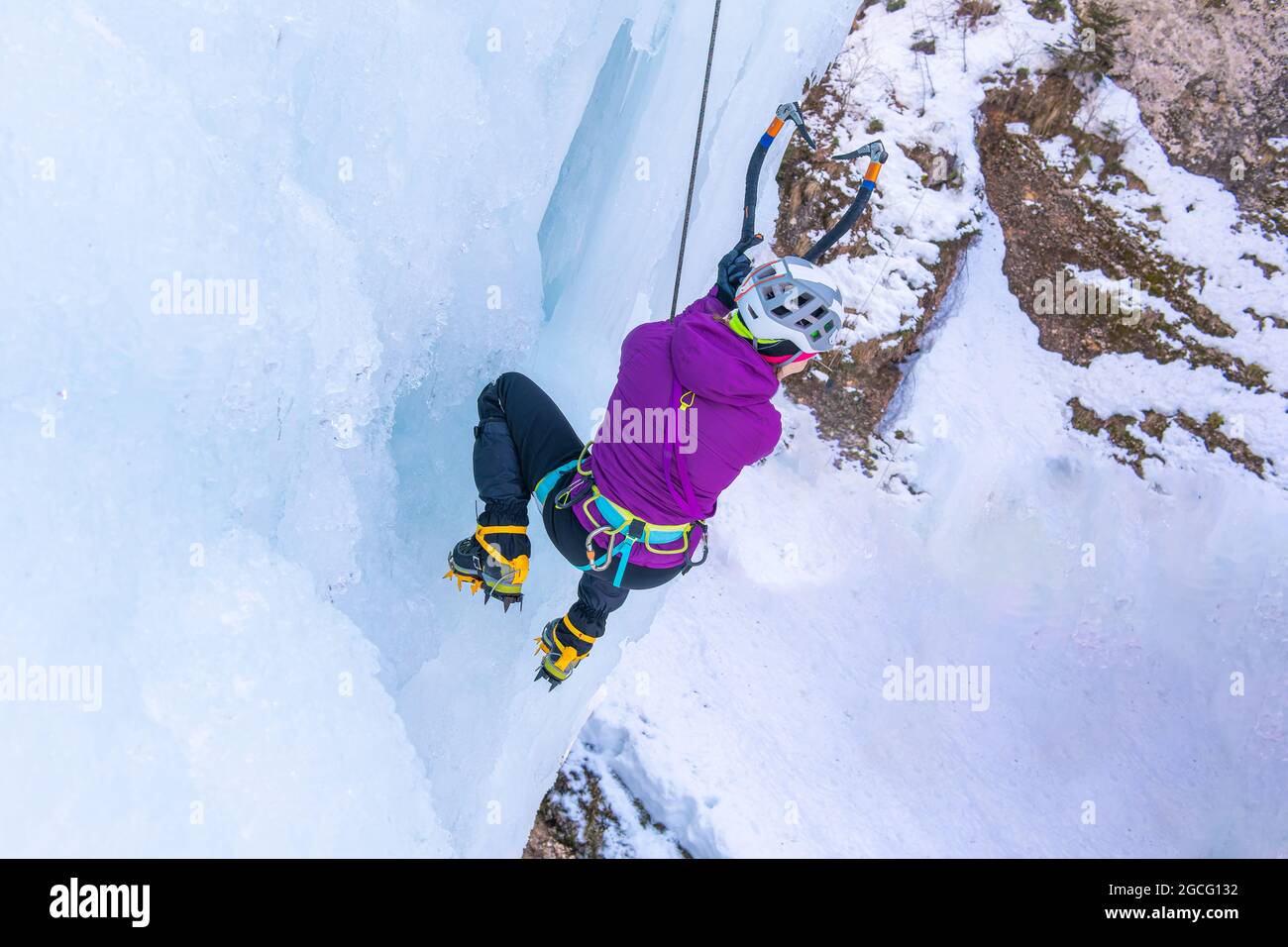 Escalador de hielo femenino caminando sobre una superficie de hielo vertical congelado, haciendo sentadilla, pie, y balanceando los movimientos de los ejes de hielo Foto de stock