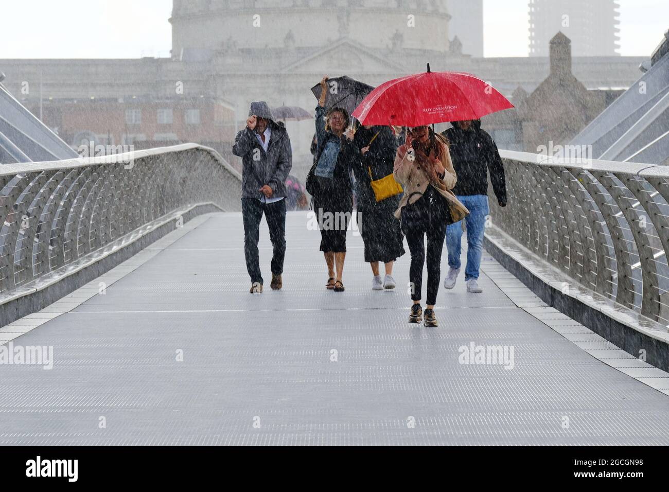 Londres, Reino Unido. La gente atraviesa el Puente del Milenio durante una fuerte lluvia, ya que el tiempo inestable continúa en la capital causando inundaciones repentinas. Foto de stock