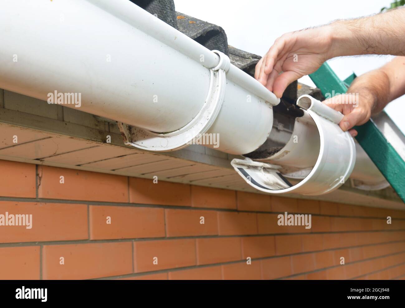 Instalación y reparación del canalón del techo. Un hombre en una escalera  está reemplazando una junta de canalón de lluvia de plástico, soporte,  conectando los canalones Fotografía de stock - Alamy