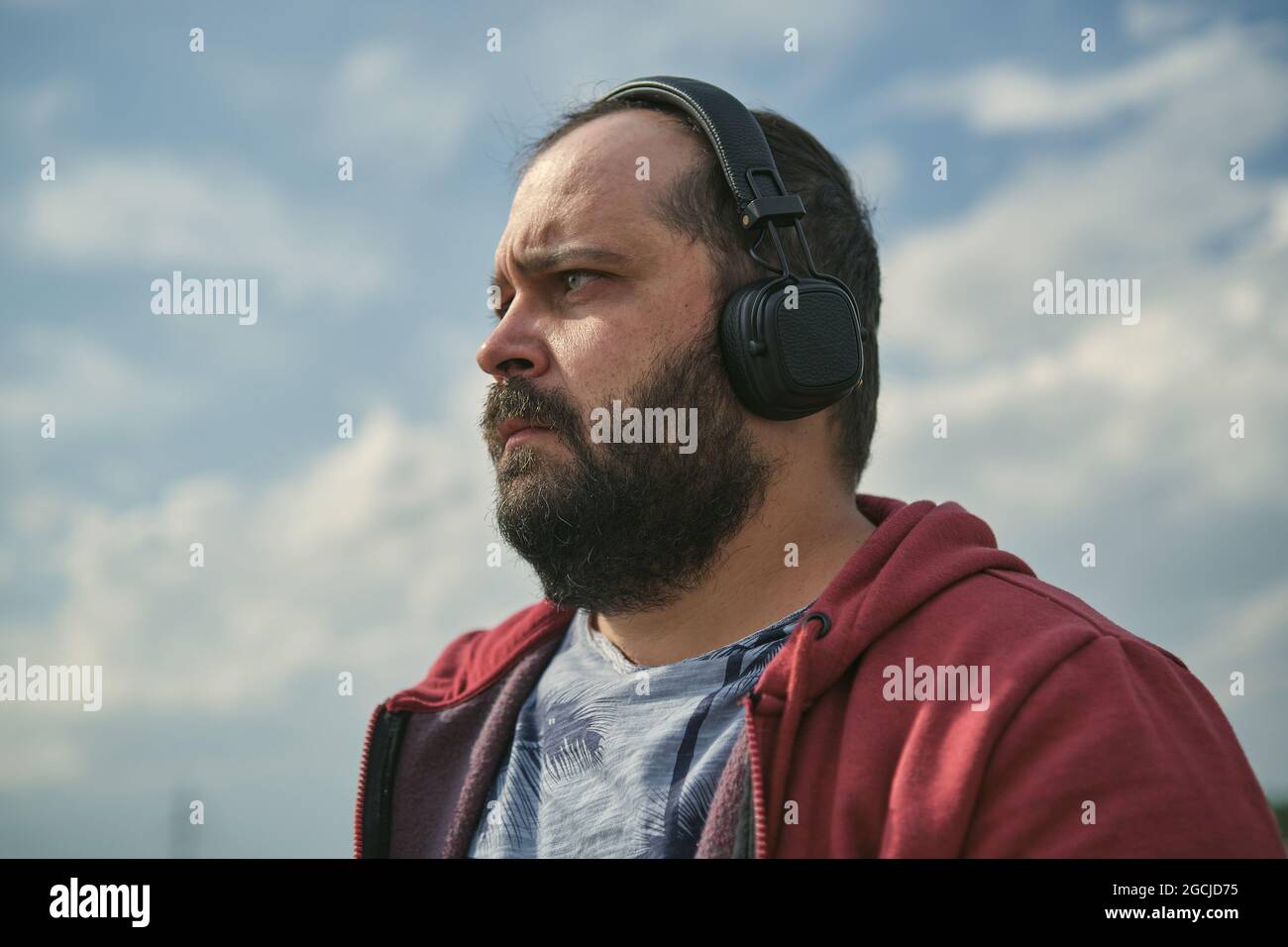 Hombre europeo de mediana edad con auriculares al aire libre escuchando música sobre el fondo del cielo Foto de stock