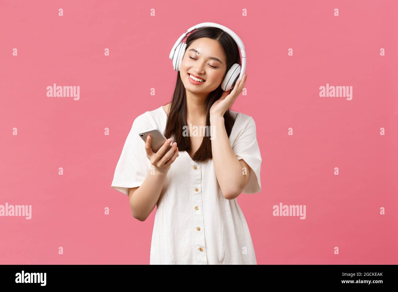 Belleza, emociones de la gente y concepto de tecnología. Chica sexy y  asiática bonita y sin preocupaciones disfrutando de la música en  auriculares inalámbricos, los ojos cerrados y sonriendo Fotografía de stock  -