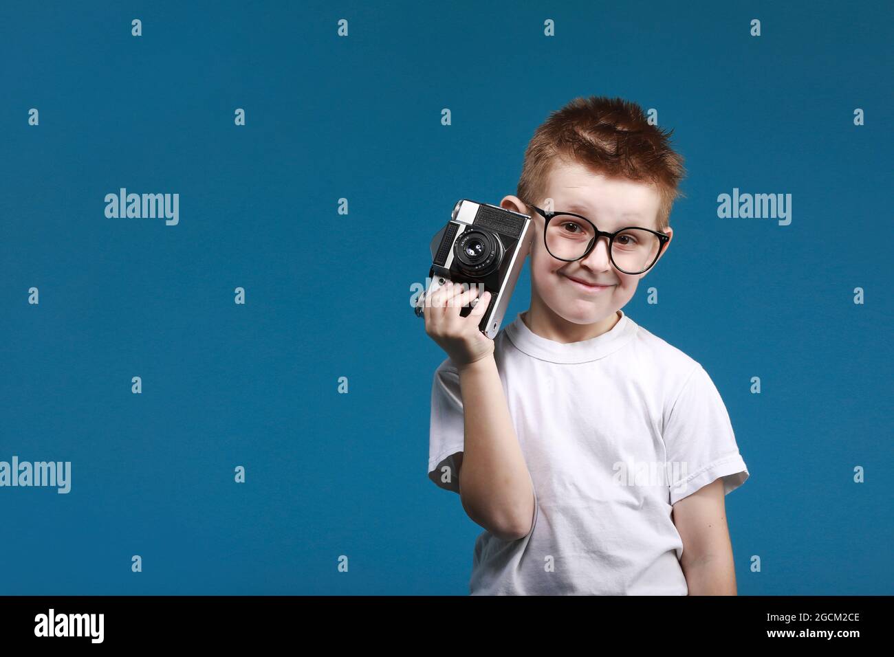 Niño pequeño tomando una foto con una cámara retro. Niño niño con cámara  fotográfica vintage aislada sobre fondo azul. Antiguo concepto tecnológico  con espacio de copia. Fotografía de aprendizaje infantil Fotografía de