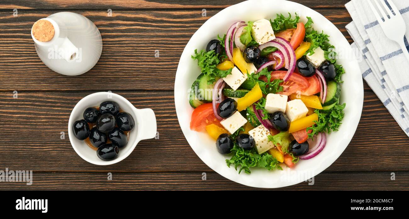 Ensalada griega tradicional de pepino fresco, tomate, pimiento dulce, lechuga, cebolla roja, queso feta y aceitunas con aceite de oliva sobre plato blanco. Sano foo Foto de stock