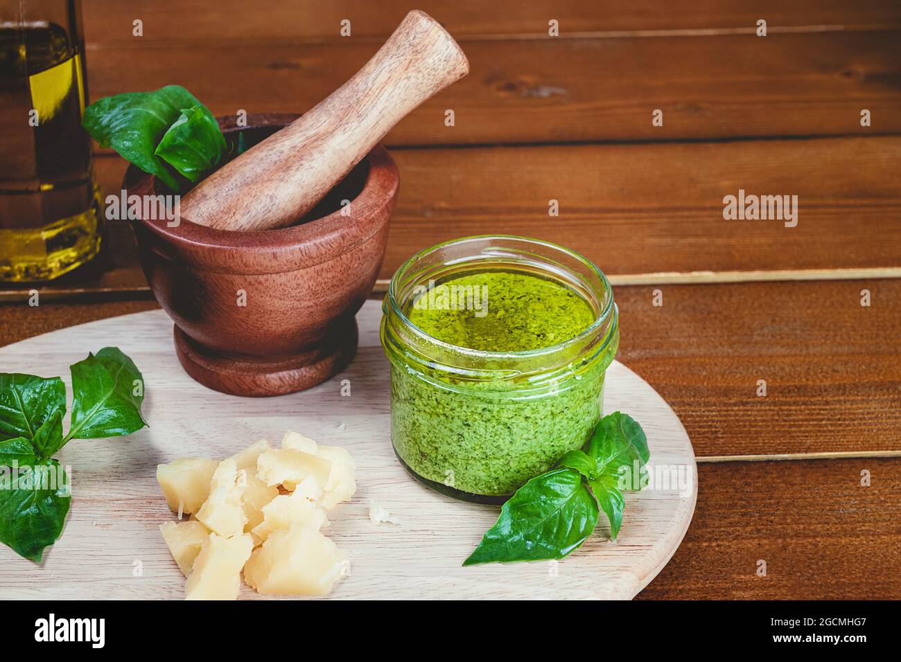 Ingredientes de la receta Pesto salsa italiana. Salsa de pesto verde casera  con albahaca, piñones, ajo, limón, aceite de oliva y mortero de madera  sobre mesa de madera bac Fotografía de stock -