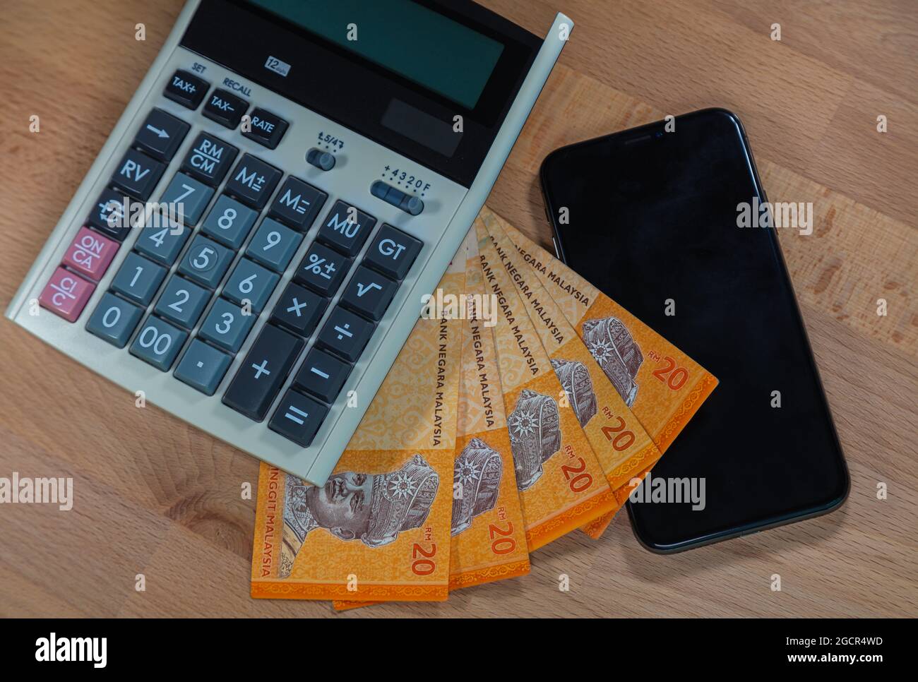 20 Ringgit malasio sobre un escritorio de madera, rodeado de calculadora y teléfono móvil. Primeros planos macro fotografía de dinero y servicios públicos de oficina Foto de stock