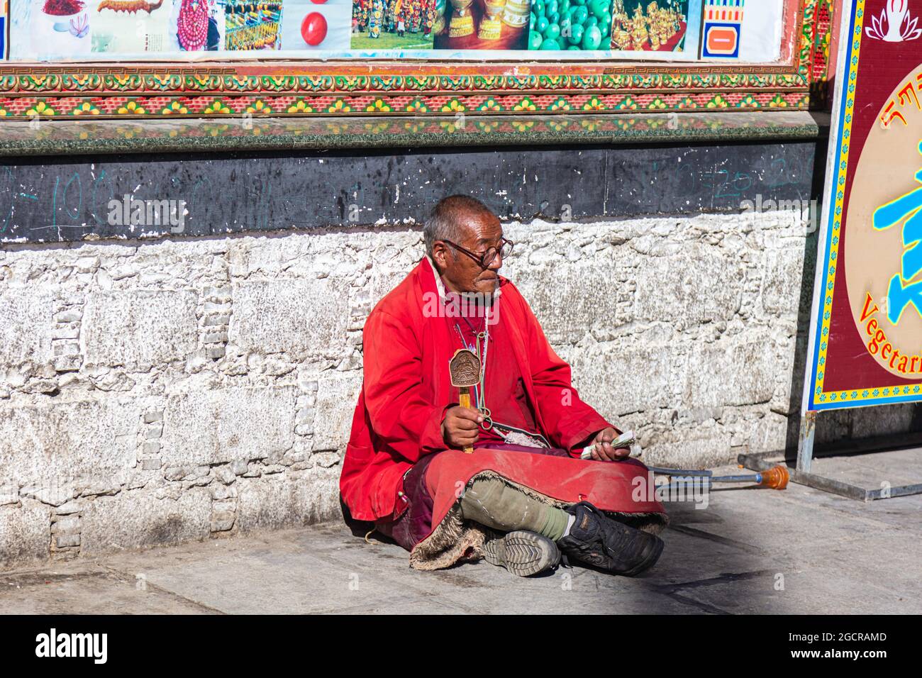 Lhasa, Tibet, China - 15 de noviembre de 2019: Viejo tibetano con muletas y rueda de oración tibetana sentado en el lado de la carretera cerca del templo Jokhang. El Foto de stock