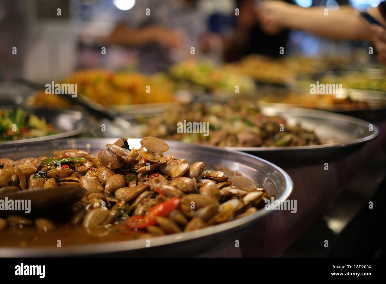 Visita al mercado nocturno en Tailandia: Un puesto de comida con platos de metal llenos de conchas fritas con especias, y otras comidas tradicionales tailandesas Foto de stock