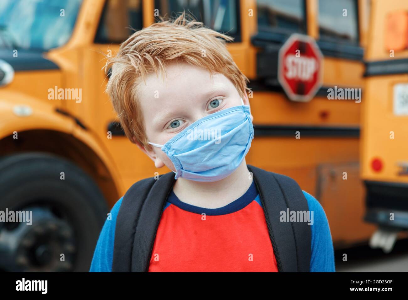 Niño niño estudiante en la máscara protectora de la cara cerca de la escuela autobús amarillo al aire libre. Nueva normalidad en la pandemia de coronavirus covid-19. Mediciones contra virus sprea Foto de stock