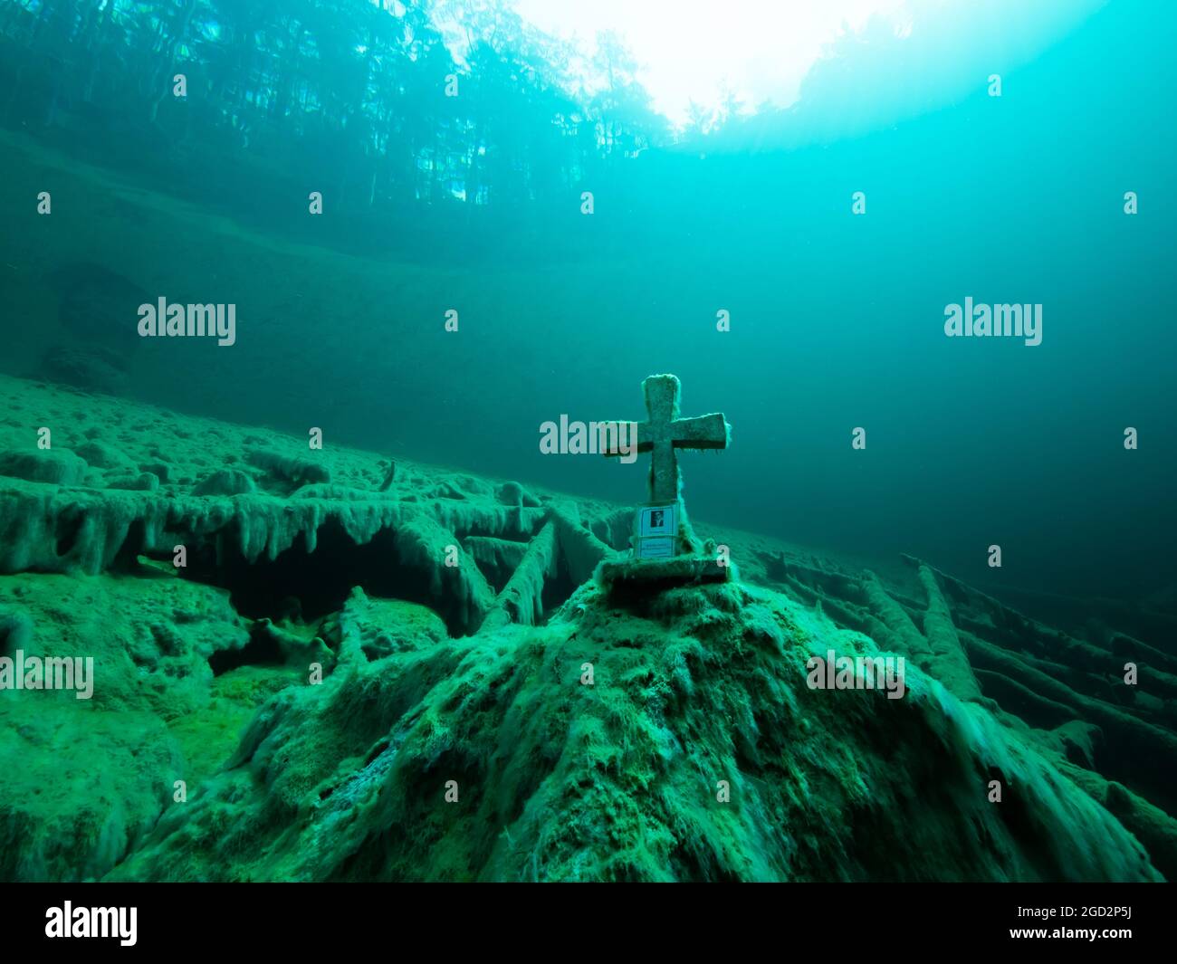 Cruz de piedra bajo el agua en un lago de montaña, buena visibilidad, agua clara y algunos troncos de árboles bajo el agua, reflejo de un bosque en la superficie del agua, Foto de stock