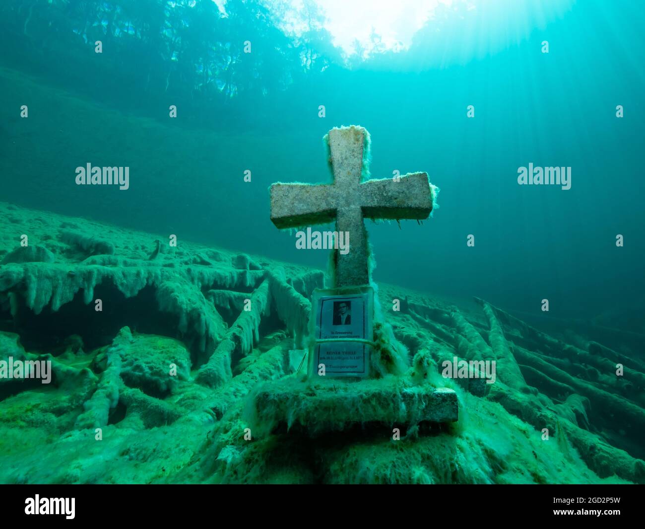 Cruz de piedra bajo el agua en un lago de montaña, buena visibilidad, agua clara y algunos troncos de árboles bajo el agua, reflejo de un bosque en la superficie del agua, Foto de stock
