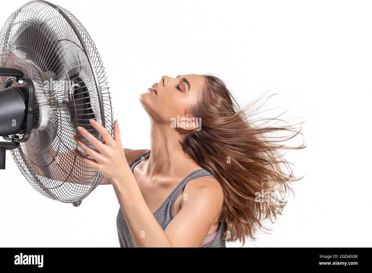 Mujer joven enfriándose con ventilador eléctrico en verano caliente aislado sobre fondo blanco Foto de stock