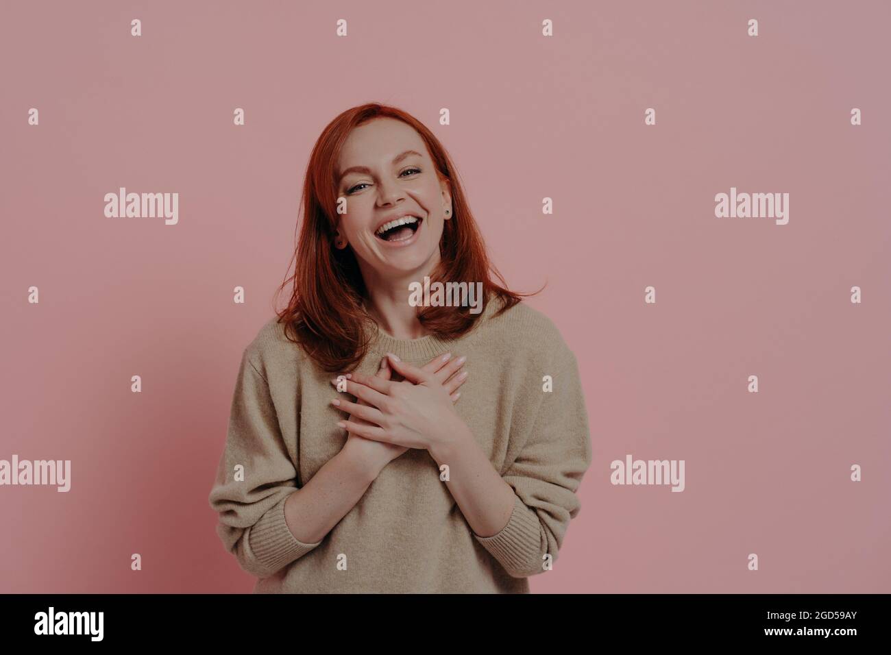 Mujer divertida de pelo rojo encantada riendo en voz alta aislada sobre fondo rosa Foto de stock