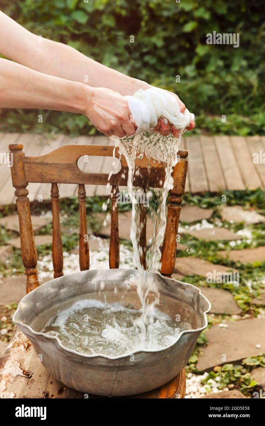 Foto recortada de mujer lavando ropa sucia en la cuenca de metal en el día  soleado cerca de casa, hembra apretando paño blanco húmedo sobre el  recipiente con agua de espuma Fotografía