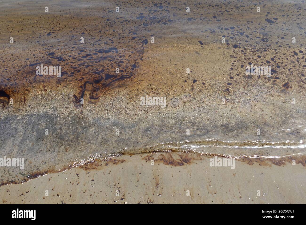 Aceite de alquitrán negro flotando sobre el agua de mar de la playa de arena contaminada. Foto de stock