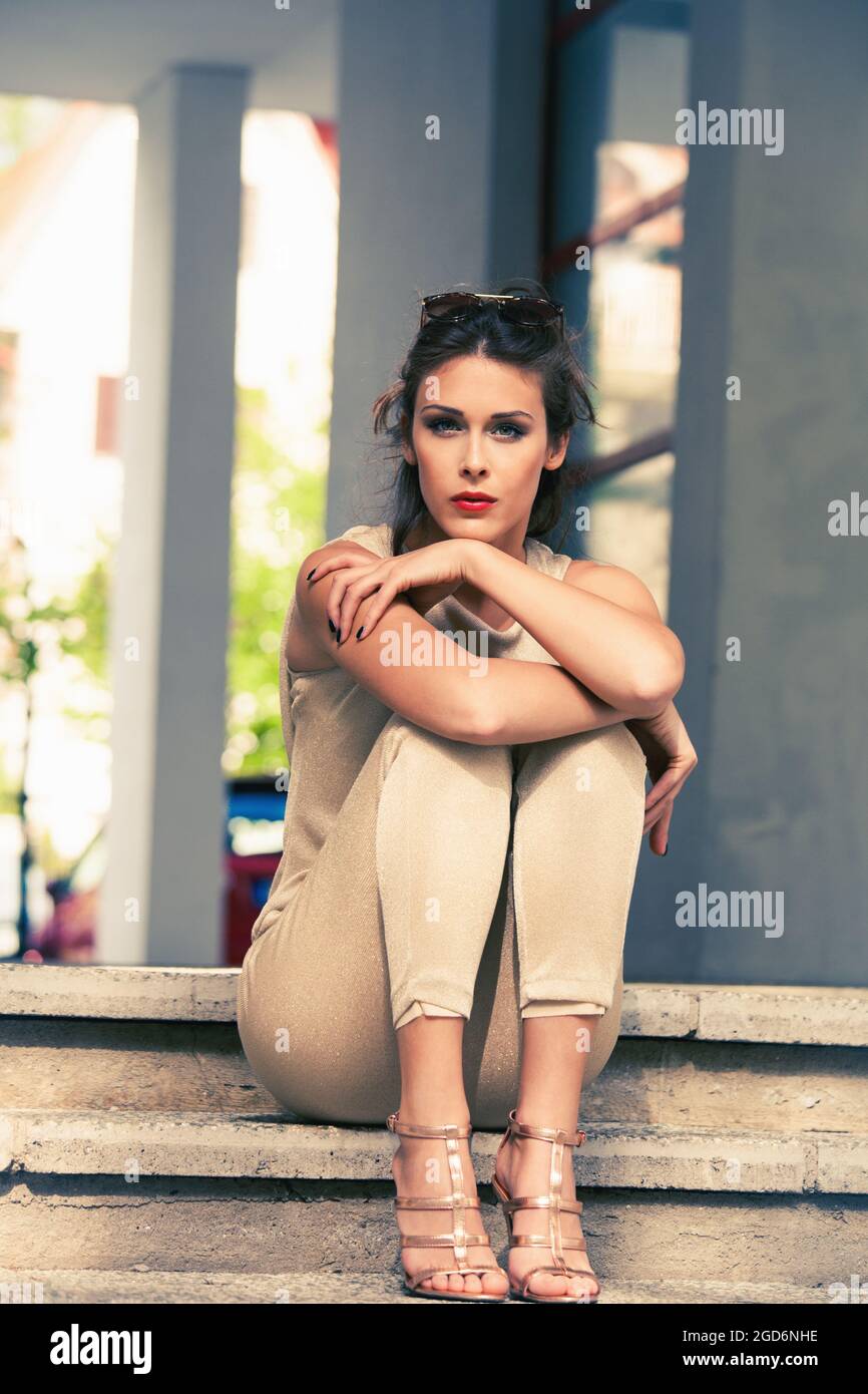 una mujer joven con pantalones dorados y sandalias se sienta en las  escaleras Fotografía de stock - Alamy