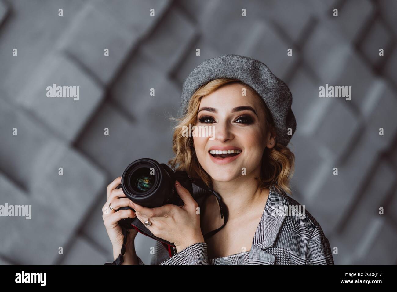 Retrato de una bella y elegante mujer fotógrafa con un traje gris con una  cámara en sus manos en un estudio fotográfico. Enfoque selectivo suave.  Espacio de copia Fotografía de stock -