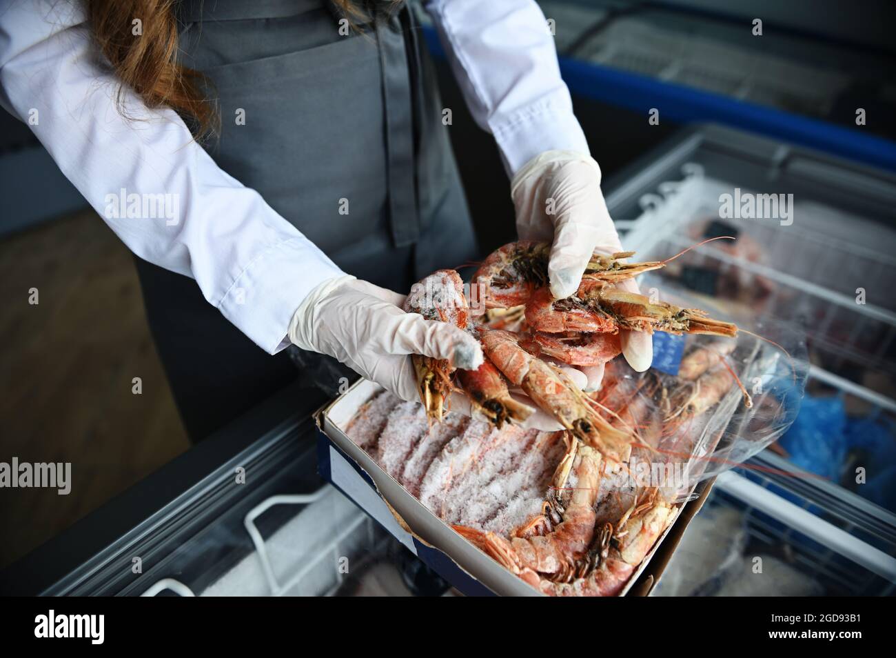 Primer plano de las manos con guantes de goma de una pescadería en una  tienda de pescado, sacando enormes gambas congeladas del frigorífico llenas  de mariscos congelados del océano. Hig Fotografía de