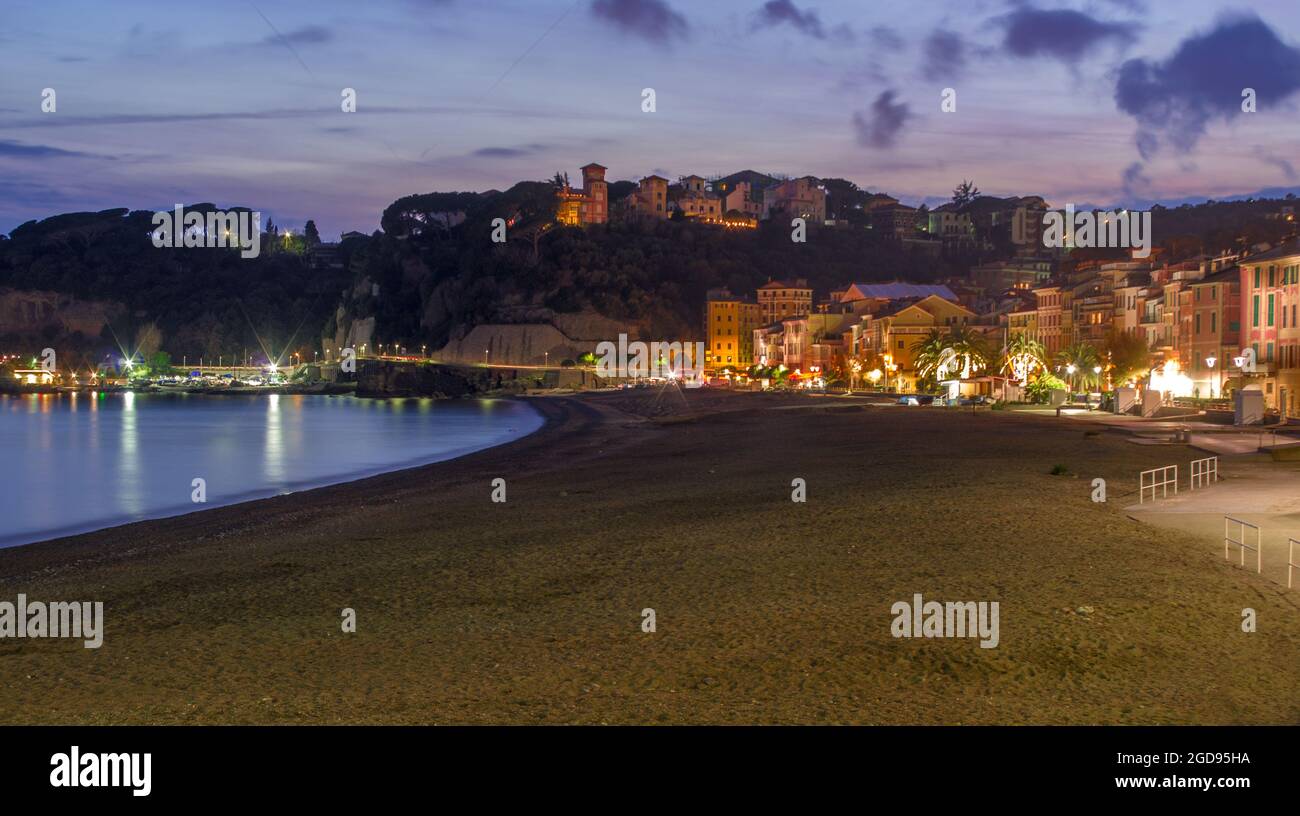 Puesta de sol sobre el pueblo iluminado y playa desierta.Celle Ligure, Italia. Foto de stock