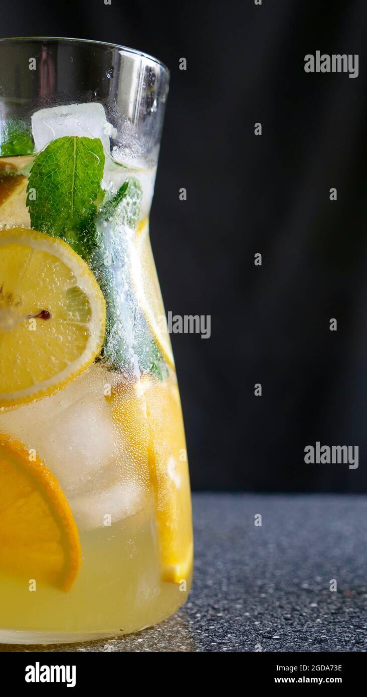 Limonada de limón con menta, limón y hielo en una jarra y un vaso con tubos de plástico negro sobre fondo de fruta. Refrescante, refrescante, fruta, bebida de verano. Primer plano vertical Foto de stock