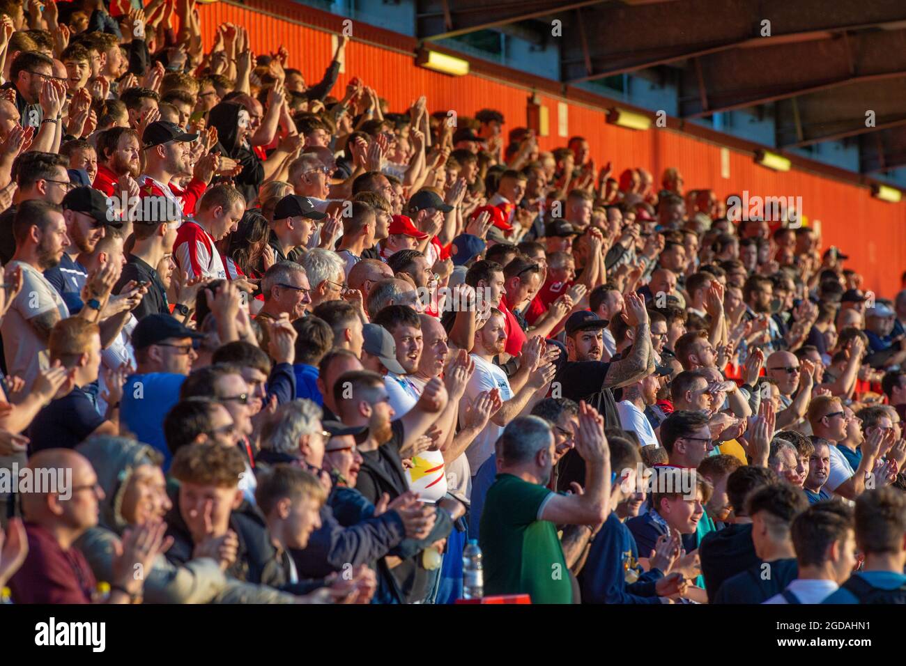Aficionados al fútbol o al fútbol aplaudiendo en un estadio iluminado por el sol Foto de stock