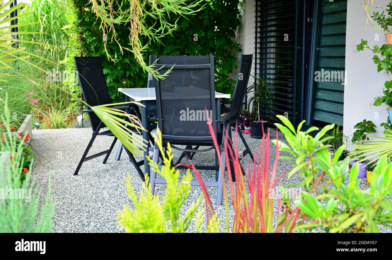 patio de la casa al aire con suelo de moqueta de piedra, flores y plantas verdes en crecimiento, y mesa con sillas. Casa terraza cubierta plantas de stock -