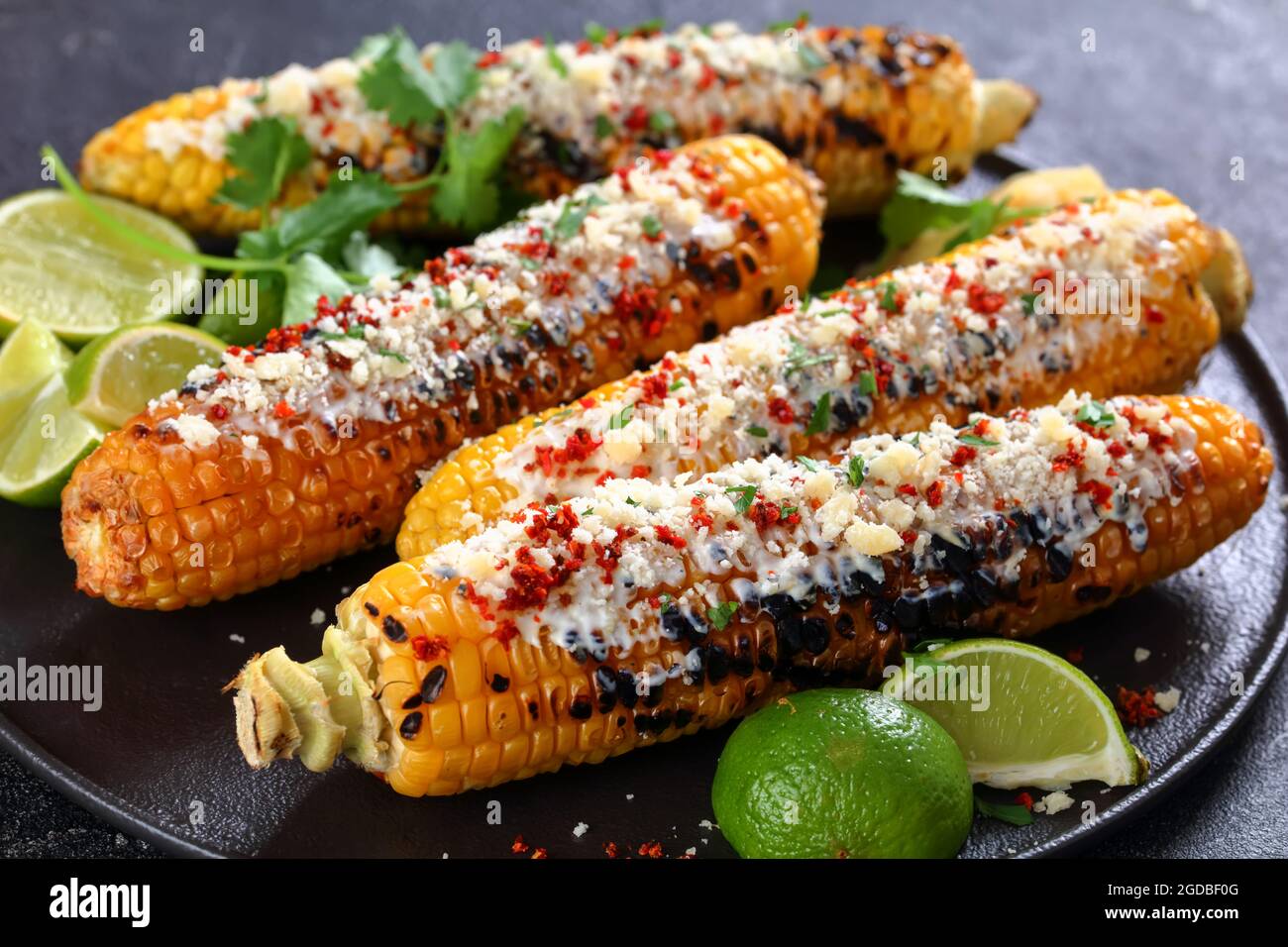 Elote, maíz de calle mexicano a la parrilla, mazorcas carbonizadas son  semplumadas en salsa a base de crema agria, condimentadas con chile en  polvo y rociadas con queso, cillante Fotografía de stock -