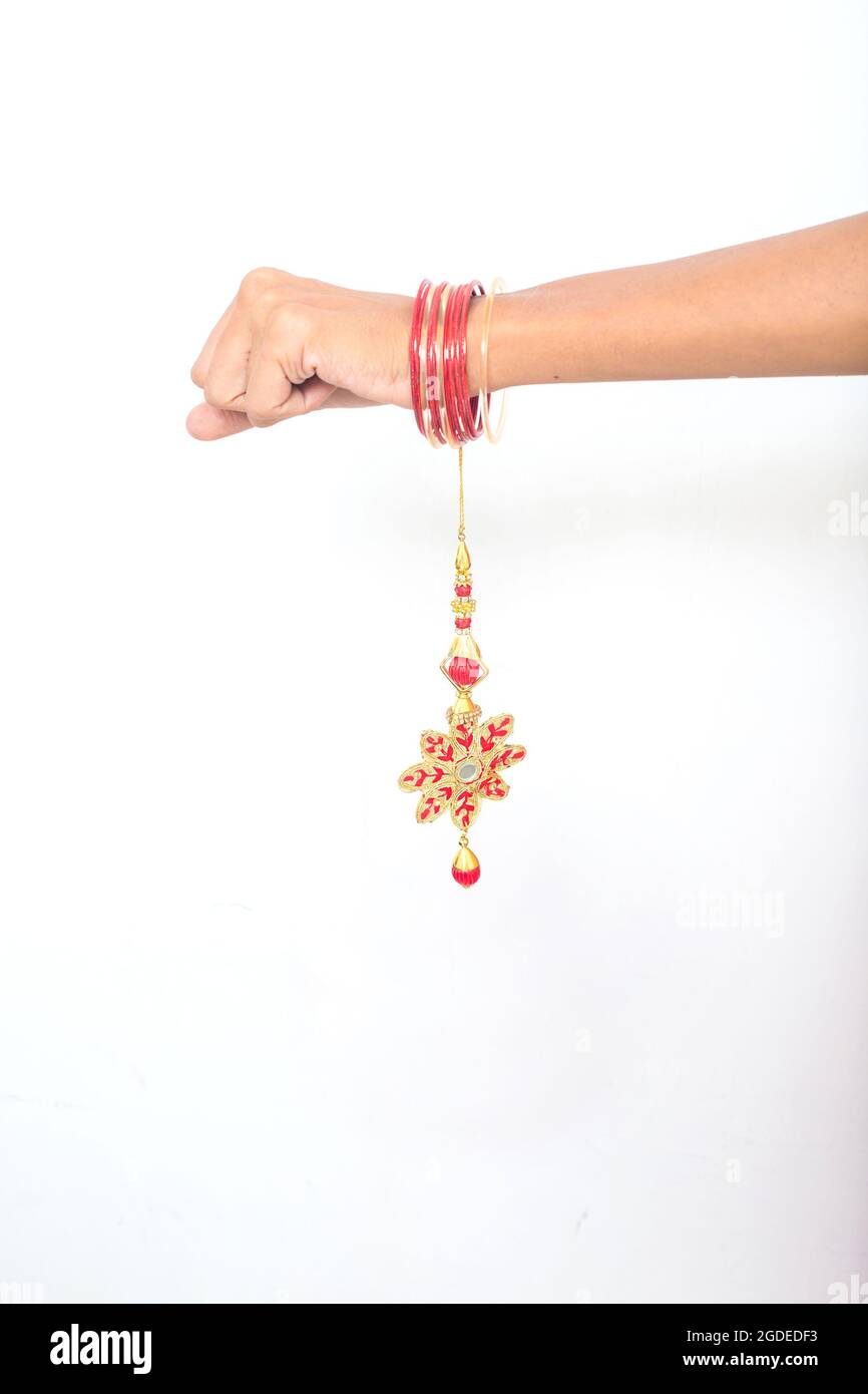 Mano femenina con hermoso color rojo lumba rakhi en la ocasión de raksha bandhan sobre fondo blanco. Pulsera de diseño floral hilo de seda, festival indio Foto de stock