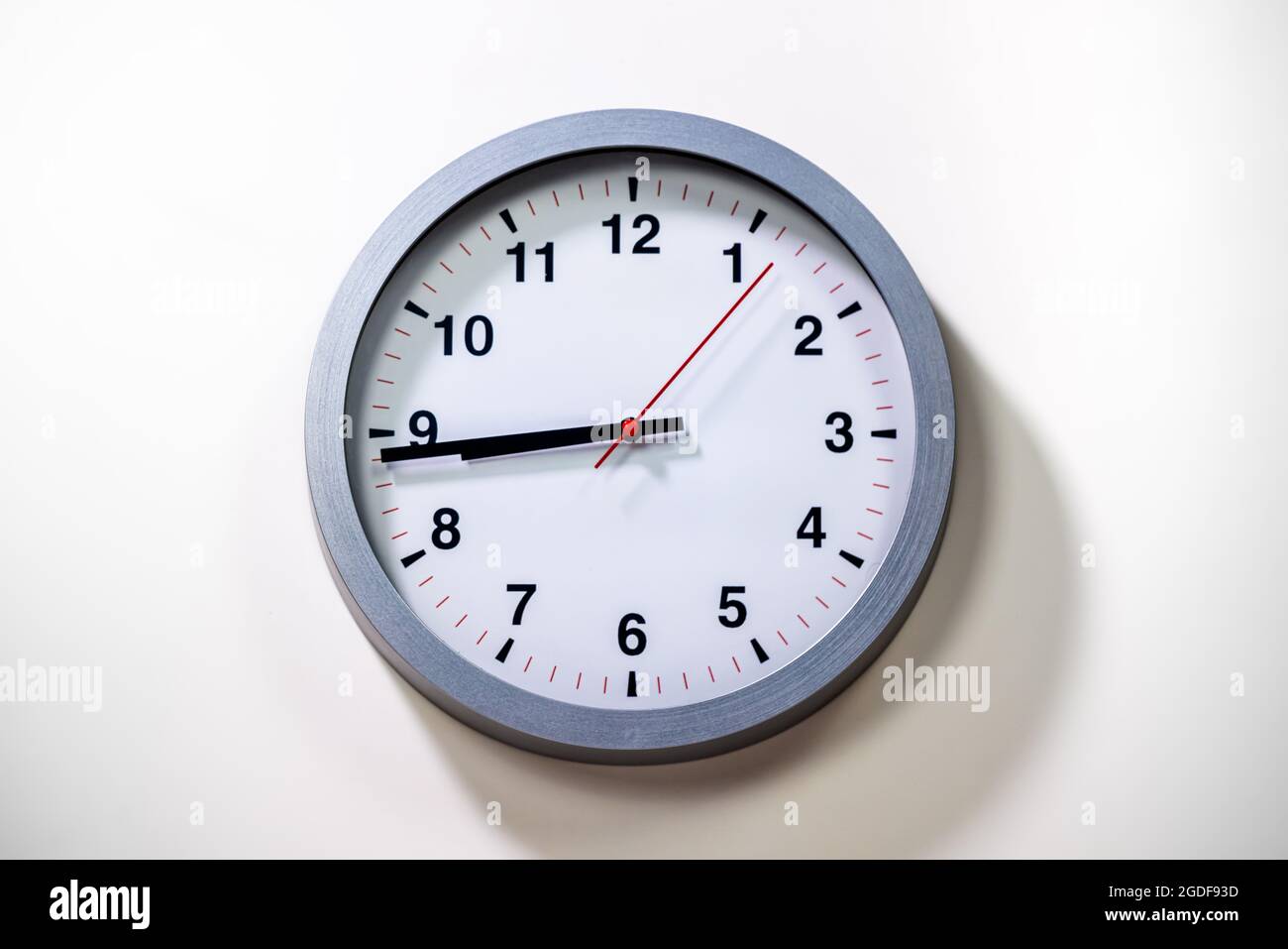 El reloj de pared gris muestra la hora. Moderno reloj de pared con marco gris sobre fondo blanco. Cerca de un reloj, con un puntero de tiempo negro y un segundo poin rojo Foto de stock