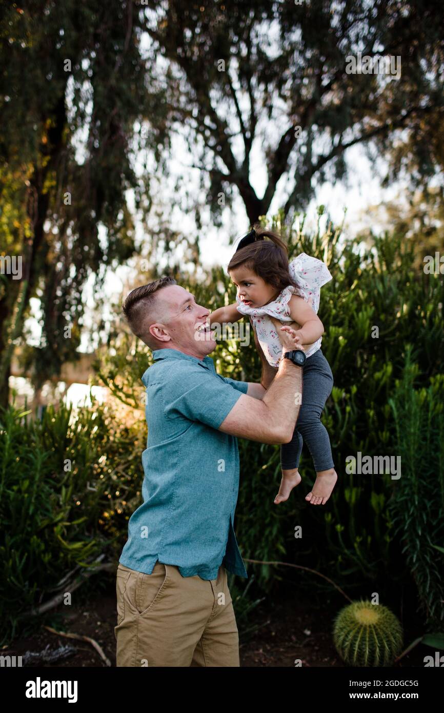 Papá militar que eleva a la hija joven en el aire en San Diego Foto de stock