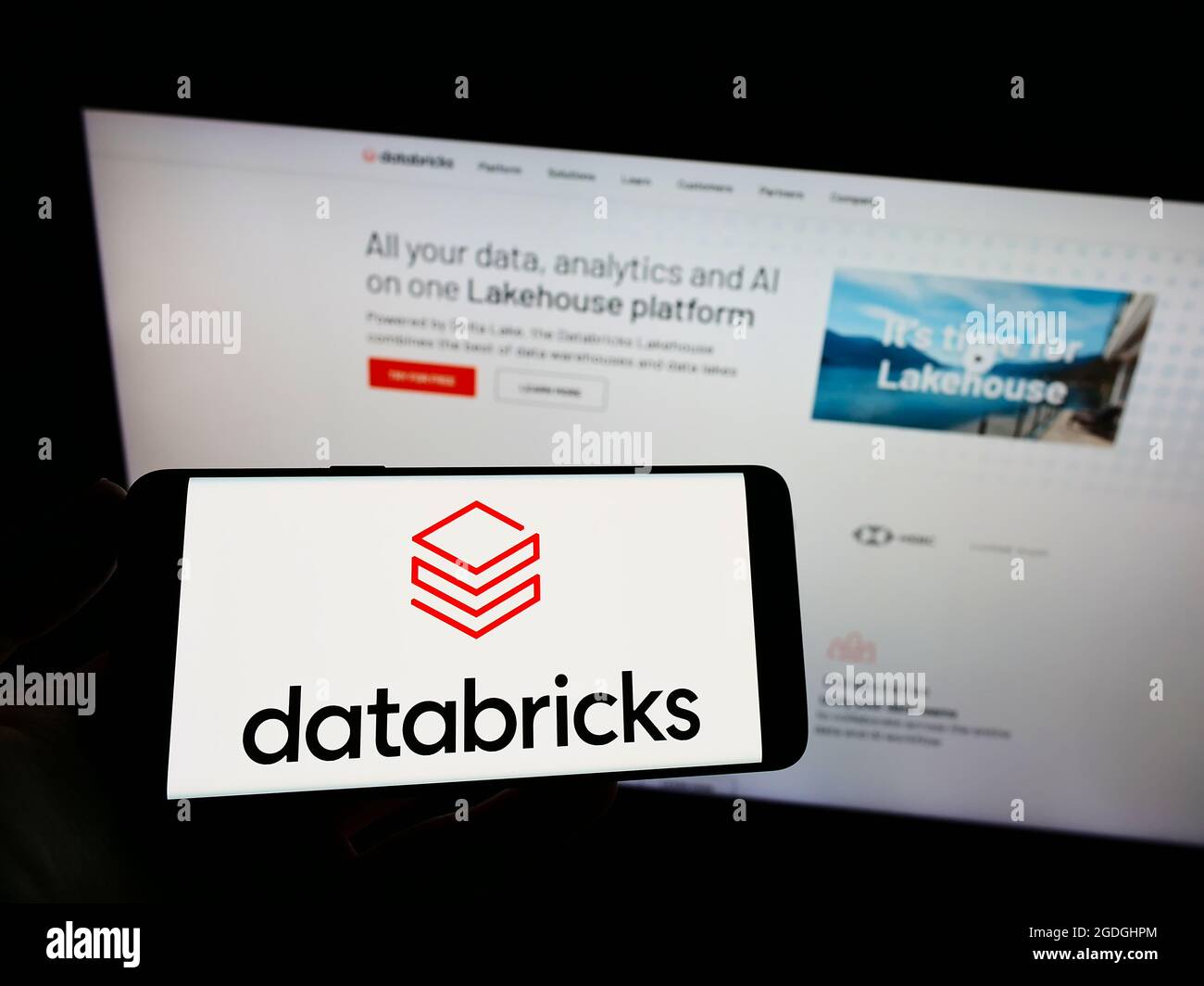 Persona que sostiene el teléfono móvil con el logotipo de la empresa estadounidense Databricks Inc. En la pantalla frente a la página web de la empresa. Enfoque en la pantalla del teléfono. Foto de stock