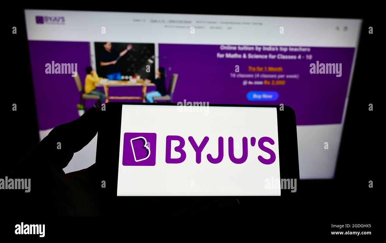 Persona con smartphone con el logotipo de la empresa india de e-learning Byju en la pantalla frente al sitio web. Enfoque en la pantalla del teléfono. Foto de stock