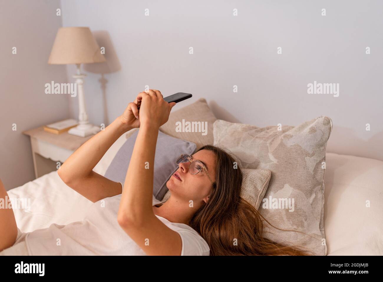 Joven latina con teléfono móvil tumbada en la cama Foto de stock
