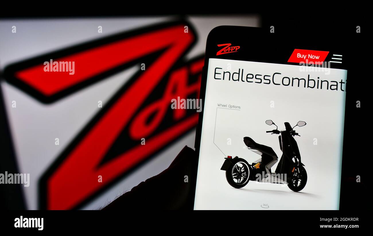Persona sosteniendo el teléfono móvil con la página web de la compañía de motocicletas eléctricas Zapp Scooters Ltd en la pantalla frente al logotipo. Enfoque en el centro de la pantalla del teléfono. Foto de stock
