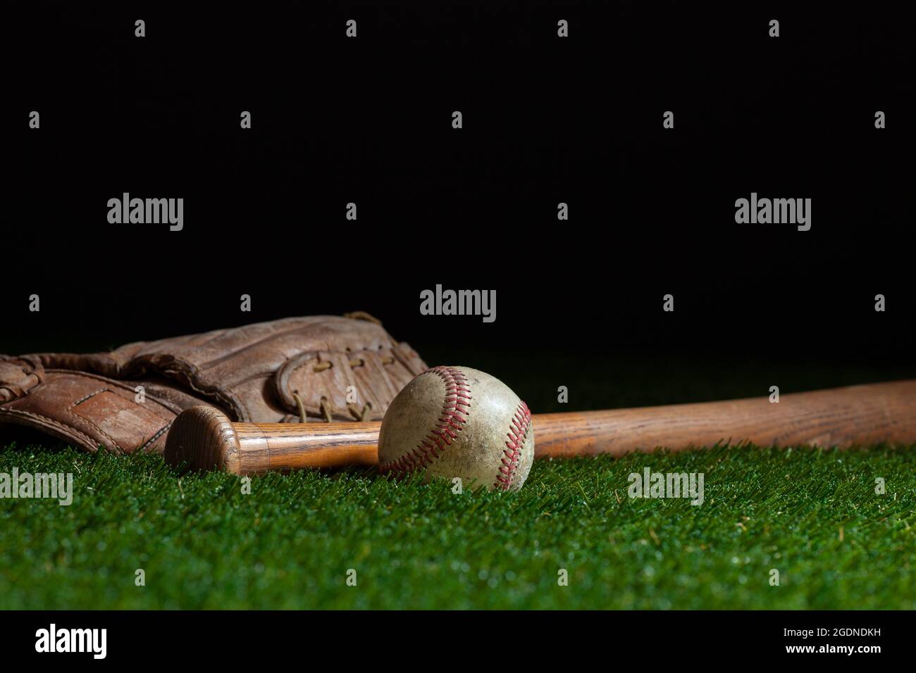 Viejo bate de béisbol y mitones enfoque selectivo de ángulo bajo en campo de hierba y fondo oscuro Foto de stock