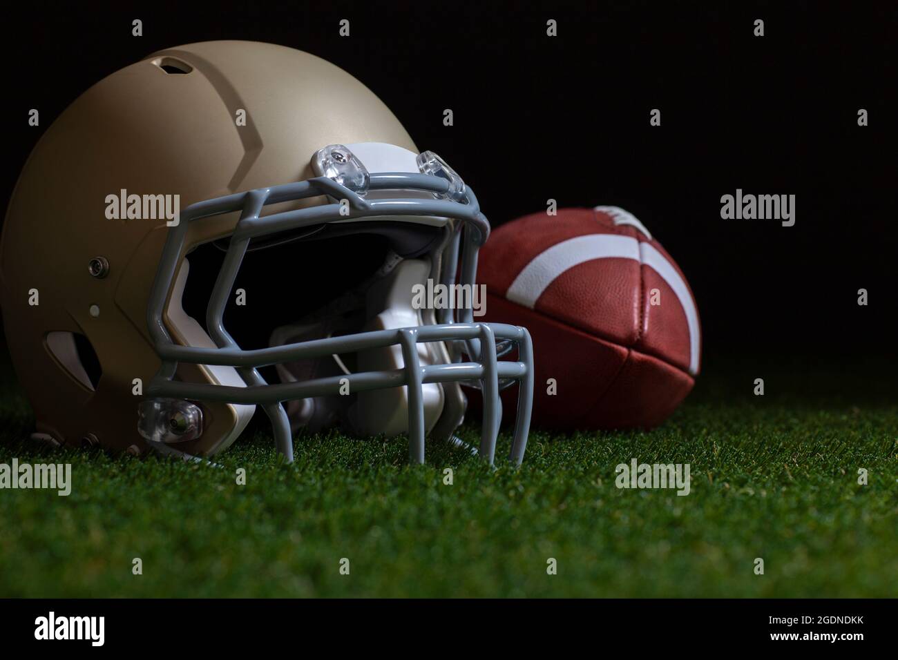 Enfoque selectivo de ángulo bajo de fútbol y casco de oro sobre hierba con fondo oscuro Foto de stock