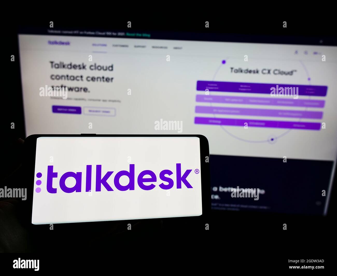 Persona que sostiene el teléfono móvil con el logotipo de la compañía de centro de contacto estadounidense Talkdesk Inc. En la pantalla frente a la página web. Enfoque en la pantalla del teléfono. Foto de stock