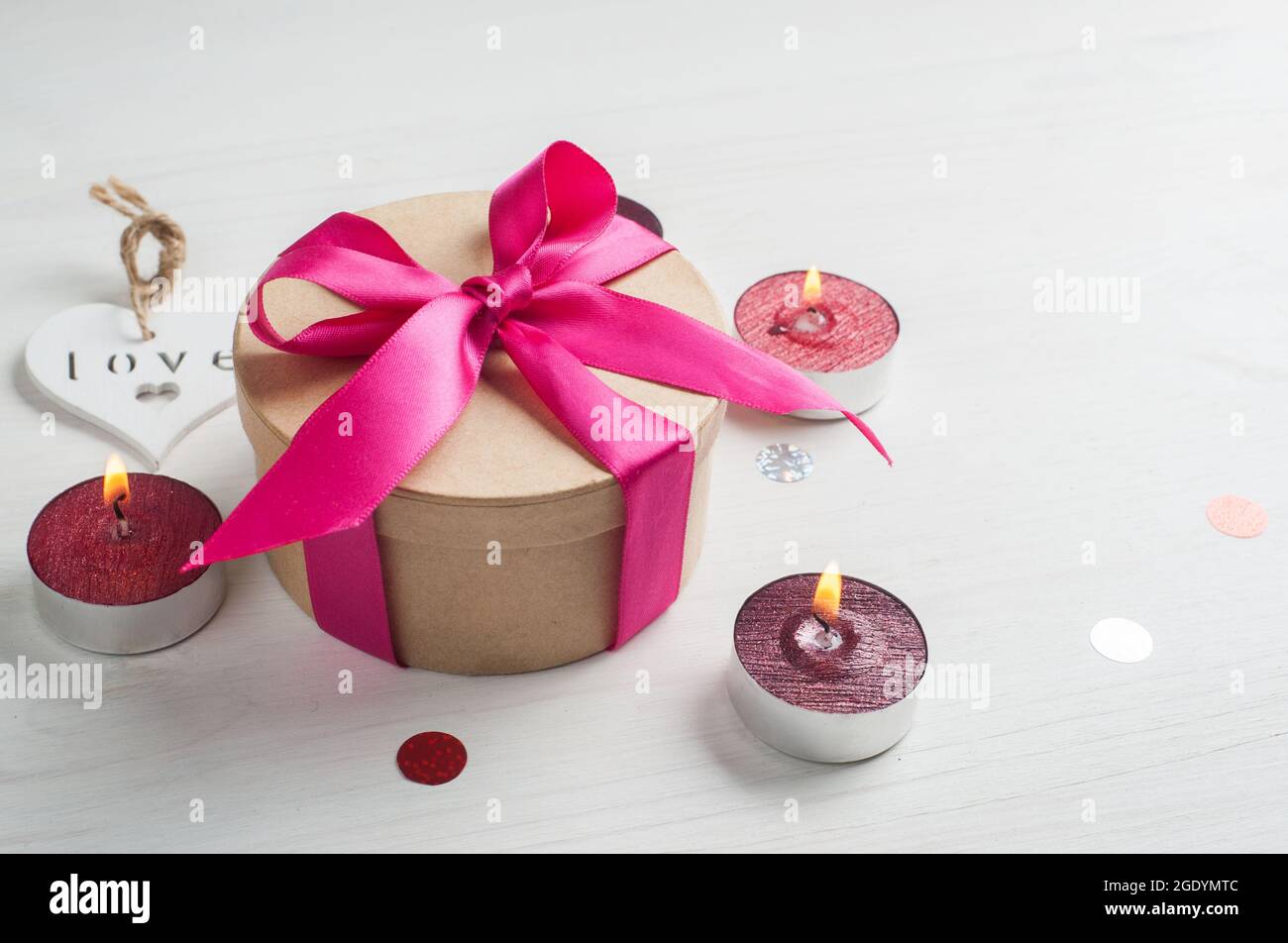Caja de regalo con lazo rosa y velas encendidas, vista con espacio de copia. Concepto de vacaciones de San Valentín Foto de stock