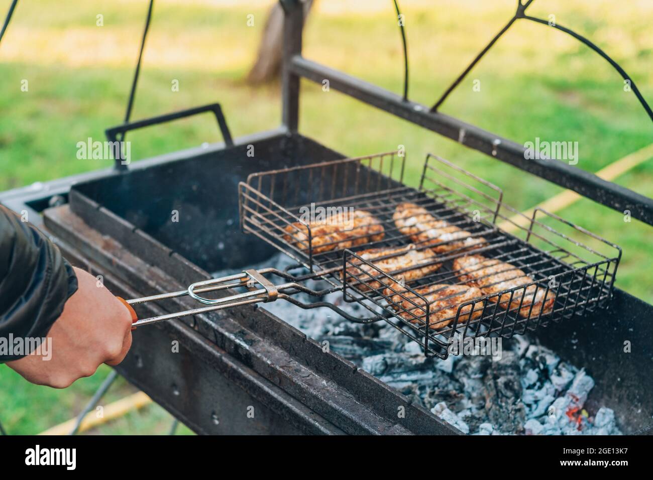 La mano masculina da vuelta a la carne frita cruda en brochetas se cocina  en parrilla de carbón. Cocinar barbacoa al aire libre Fotografía de stock -  Alamy