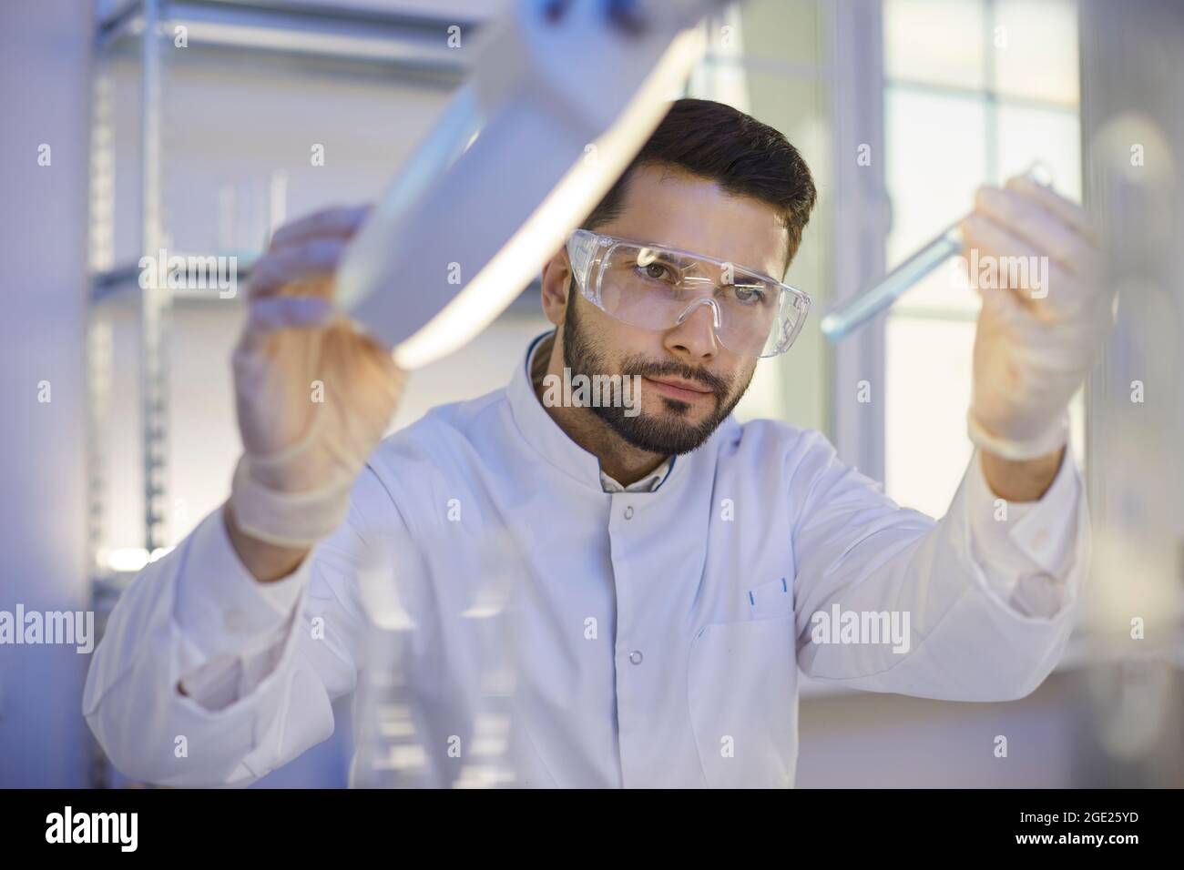 Investigador que mira con el tubo de ensayo de líquido químico bajo lámpara en el laboratorio Foto de stock