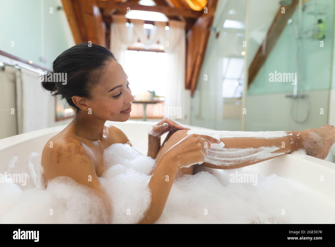 Mujer mixta de la raza en el baño con una bañera y afeitándose las piernas Foto de stock