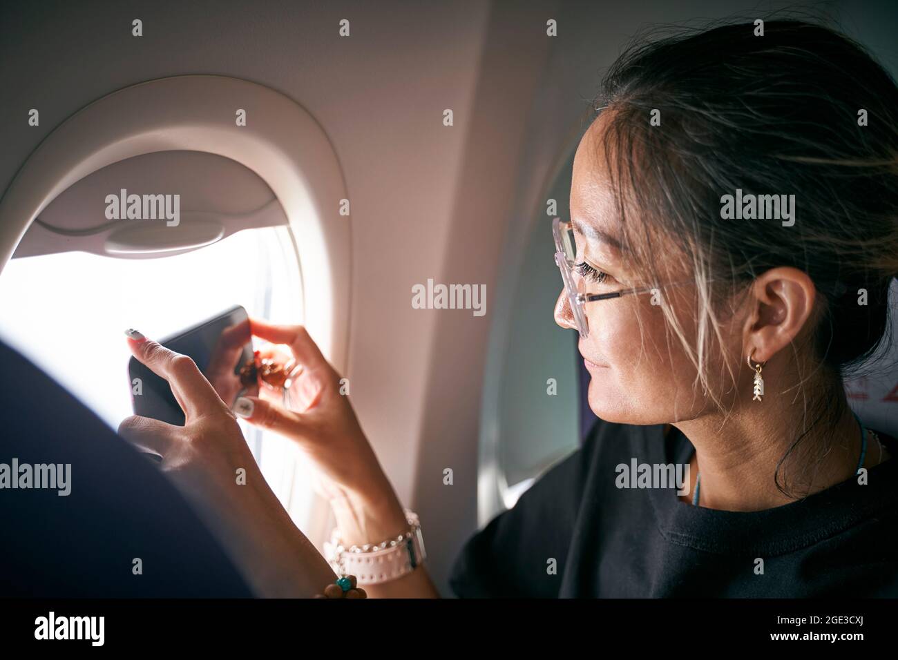 una mujer asiática que hace una foto usando el teléfono móvil en la cabina del avión Foto de stock