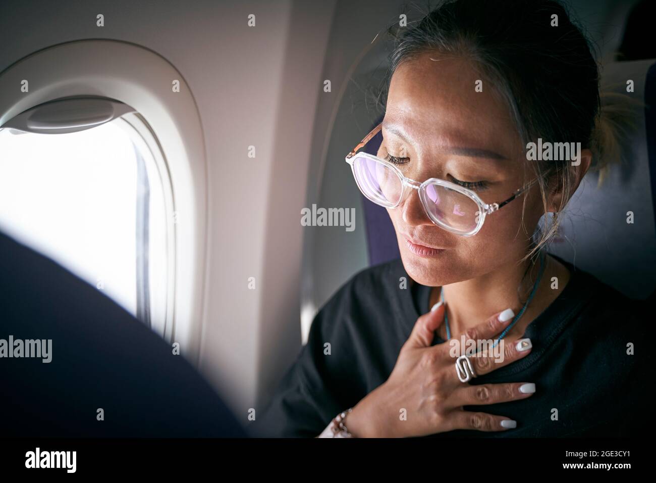 una mujer asiática de pasajeros sentada en la cabina del avión se siente incómoda Foto de stock