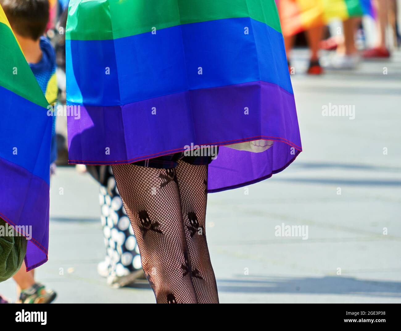 Piernas delgadas de una mujer joven de detrás con medias de red de pescado con cráneos tejidos y una capa en los colores del arco iris Foto de stock
