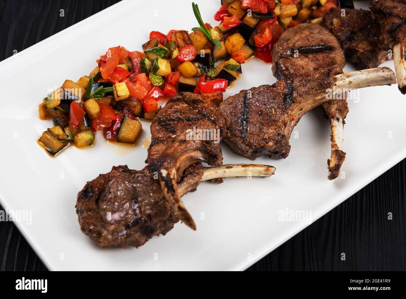 Costillas de cordero asadas con verduras sobre plato blanco sobre fondo  negro de madera Fotografía de stock - Alamy