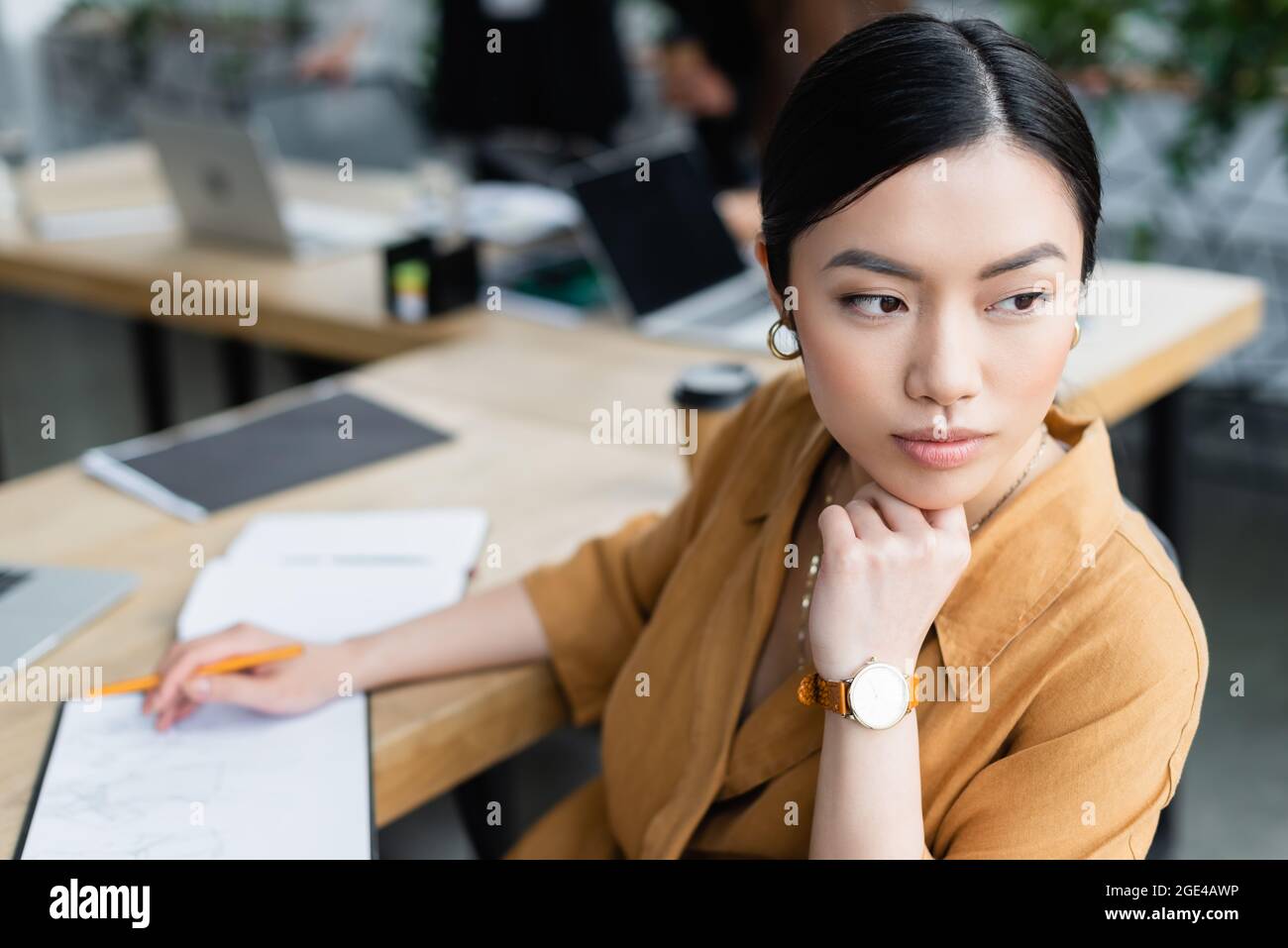 bonito diseñador asiático mirando hacia fuera mientras que piensa cerca del boceto en la oficina Foto de stock