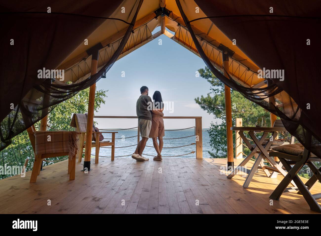 Vista trasera de una pareja amorosa de pie uno cerca del otro y mirando al océano azul mientras disfruta de las vacaciones de verano Foto de stock